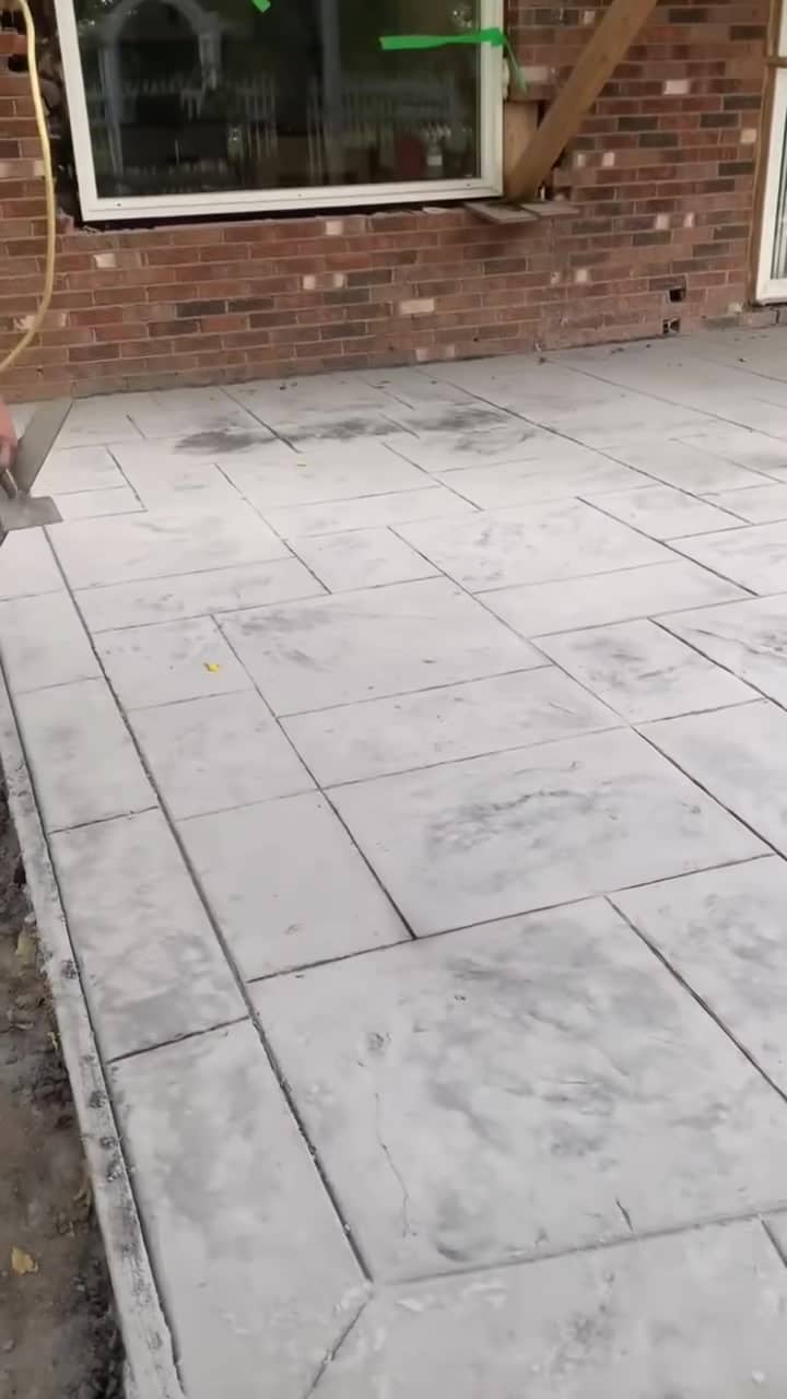 Stamped concrete patio in an interlock pattern with a smooth border beside a brick house
